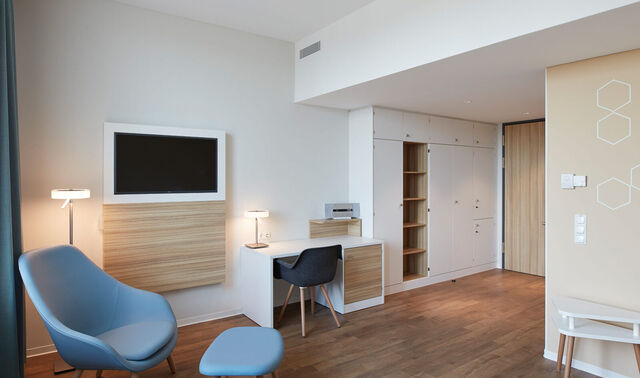 Privates Patientenzimmer. Auf diesem Bild sieht man einen Schreibtisch, einen Sessel, einen Einbauschrank und einen Fernseher.